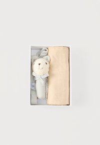 Κουτί δώρου με μια ριγέ μαλακή αρκούδα-παιχνίδι, ύφασμα με ρίγες που ταιριάζει και διπλωμένο μπεζ ύφασμα σε λευκό φόντο.