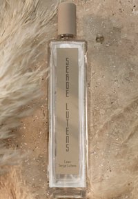 Flacone di profumo in vetro trasparente con etichetta beige caratterizzata da testo in rilievo. Coperchio arrotondato beige sulla sommità del flacone. Il testo reca la scritta "Serge Lutens."