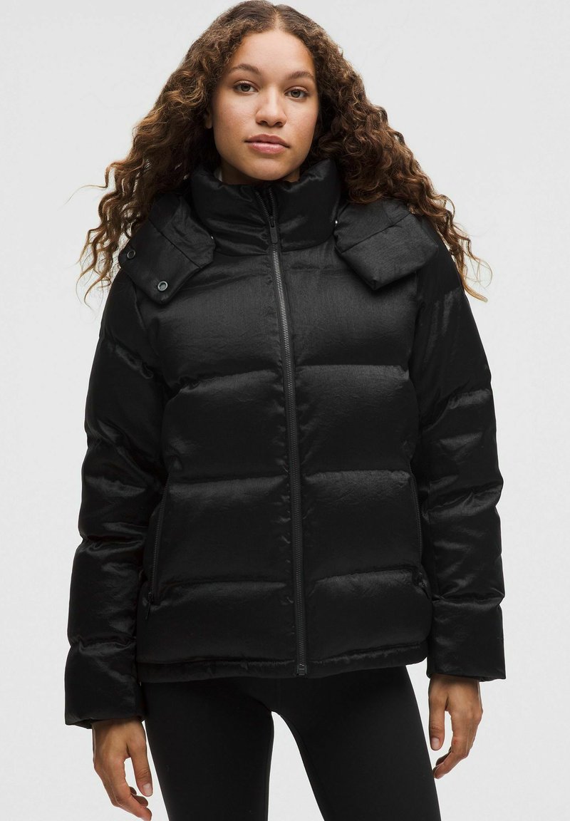 Chaqueta de plumas negra con un alto cuello, con cierre de cremallera frontal, costuras horizontales y dos bolsillos laterales. Acabado suave y brillante.