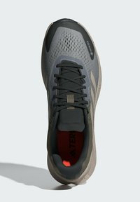 Grå löpsko med en andningsbar mesh-överdelen, svarta snören och en vadderad tunga. Den livfulla röda foder kontrasterar mot den neutrala sulan.