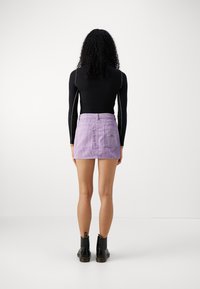 Fialová kordová minisukně s dvěma zadními kapsami, v kombinaci s upnutým černým tričkem s dlouhým rukávem a černými kotníkovými botami.