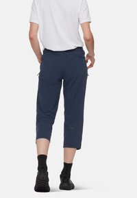 Mörkblåa capribyxor med passform, elastisk midja och blixtlås fickor; tillverkade av ett lätt och slitstarkt tyg.