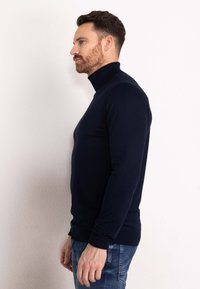 Navyblauw coltrui in een aansluitend ontwerp, gemaakt van een zacht materiaal. Bevat lange mouwen en geribbelde boorden. Gedragen met denim jeans.