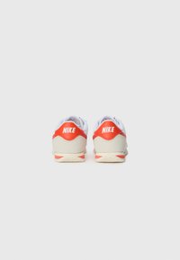 Nike tennis, mis sisaldavad valge, oranži ja beeži materjalide segu, pehme krae ja silmapaistev logo kandadel. Tekstuuriga kummist tallad.
