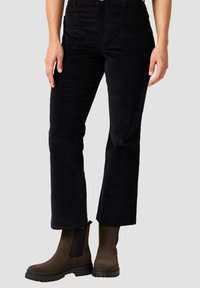 Pantalones de pana negros con un diseño de pierna recta, que cuentan con bolsillos frontales y una cintura alta, combinados con botines marrones.