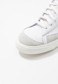 White sneaker with a textured gray suede toe cap, smooth white leather upper, and white laces; featuring a patterned rubber outsole.