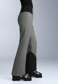 Szürke nadrág textúrált mintával, fekete díszítő panelek és fitted derékpánt. Fekete lábbelivel párosítva, amely fémes kiegészítőkkel rendelkezik.