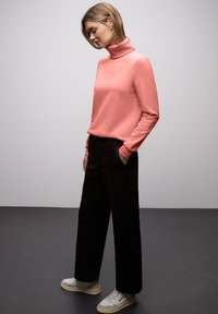 Pull à col roulé corail, pantalon large noir et baskets de couleur claire. Accent sur des lignes simples et des textures douces dans une tenue décontractée.