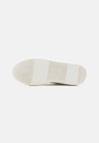 Semelle de chaussure en caoutchouc blanc avec un motif en chevron et des accents circulaires, présentant une texture lisse avec de légères variations de teinte.