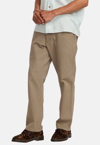 Beige cotton trousers with a straight-leg fit and front pockets, paired with black and brown leopard-print shoes. Light blue short-sleeve shirt.