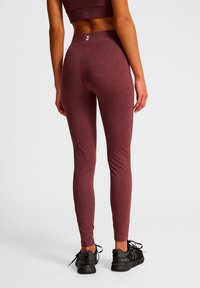 Bordeauxrode leggings gemaakt van rekbare stof met een hoge taille, een aansluitend ontwerp en chevronaccenten aan de achterkant. Gecombineerd met zwarte sneakers.