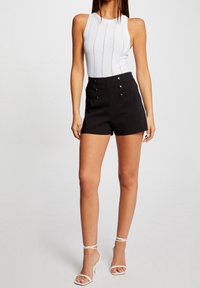 Shorts noirs taille haute avec accents à double bouton, associés à un haut sans manches blanc côtelé. Design simple et silhouette ajustée.