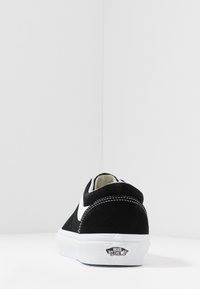 Černobílé tenisky Vans z pohledu zezadu na bílé podložce s logem "Vans Off The Wall" na patě.