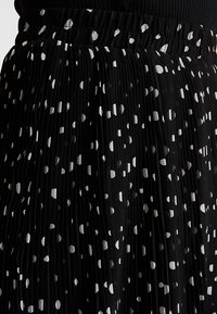 Gonna nera plissettata con motivo a pois bianchi, dotata di una vita elastica. Il tessuto ha una texture morbida e una silhouette fluida.