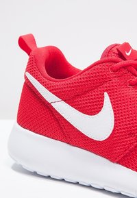 Červené sportovní boty s texturovaným textilním svrškem, bílým logem Nike a bílou gumovou podrážkou. Obsahují červený poutko na patě.