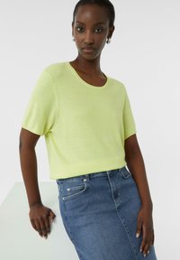 Jasnozielony sweter z krótkim rękawem i okrągłym dekoltem, zestawiony z niebieską spódnicą dżinsową. Gładka faktura i luźny krój.