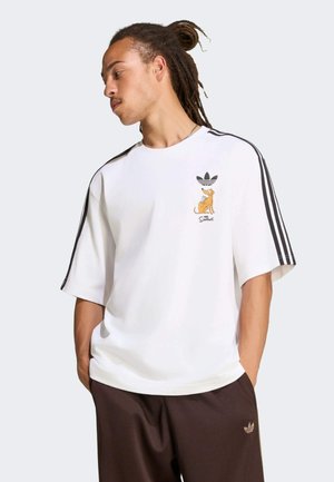 Mand med dreadlocks bærer en hvid Adidas t-shirt med sorte striber og en tegneseriehund fra The Simpsons på brystet, kombineret med mørke Adidas bukser.