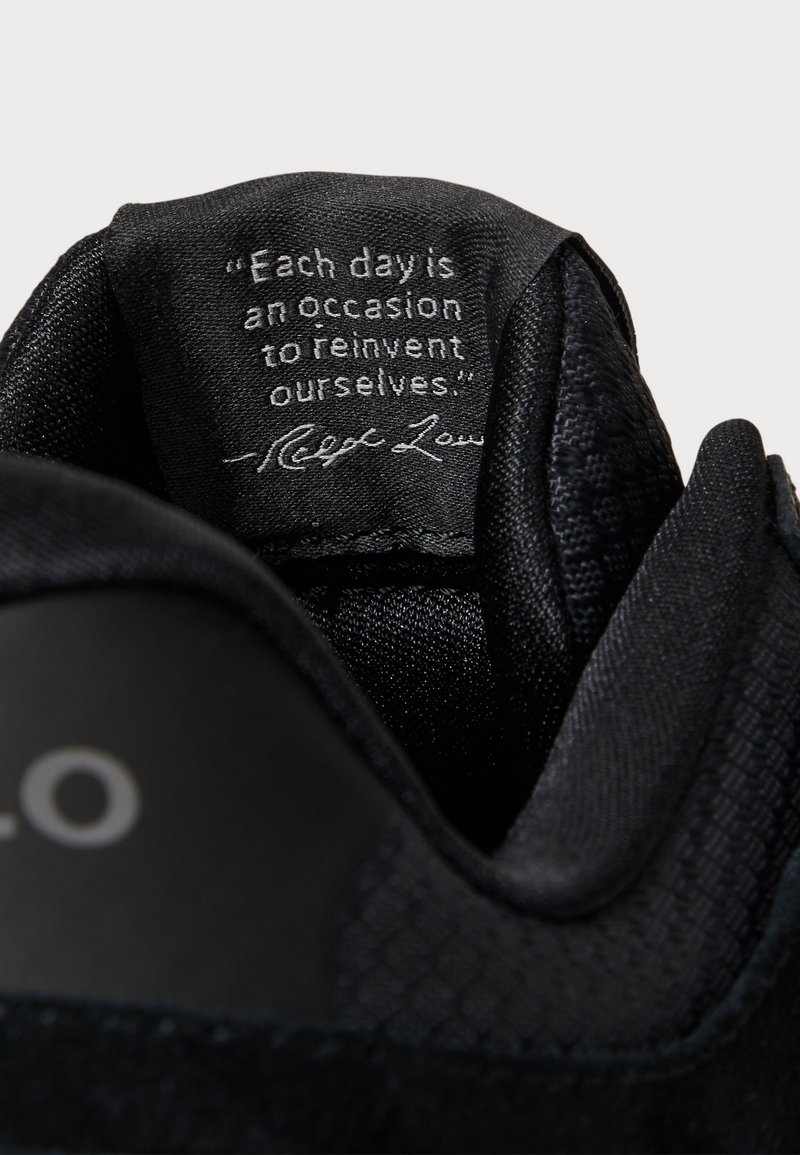 Schwarzer Sneaker-Innenbereich mit strukturiertem Stoff, ausgestattet mit einem genähten Zitat-Tag in Weiß. Der obere Rand hat eine glatte Oberfläche und ein rundes Design.