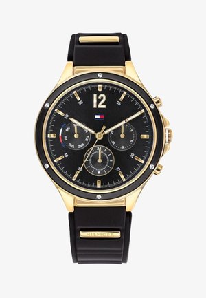 Złoty zegarek z czarną tarczą, wyposażony w trzy sub-tarczki, złote wskaźniki oraz czarny gumowy pasek. Logo marki na pasku.