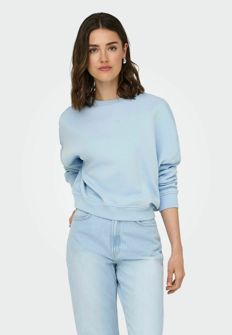 Lichtblauwe sweatshirt met een relaxte pasvorm, ribgebreide boorden en zoom, gecombineerd met lichte spijkerbroek met rechte pijpen en klassieke zakken.