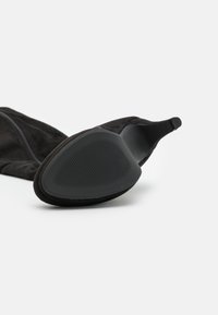 Black suede ankle boot with a rounded toe, slim heel, and textured rubber outsole. Features a side zipper for easy wear.