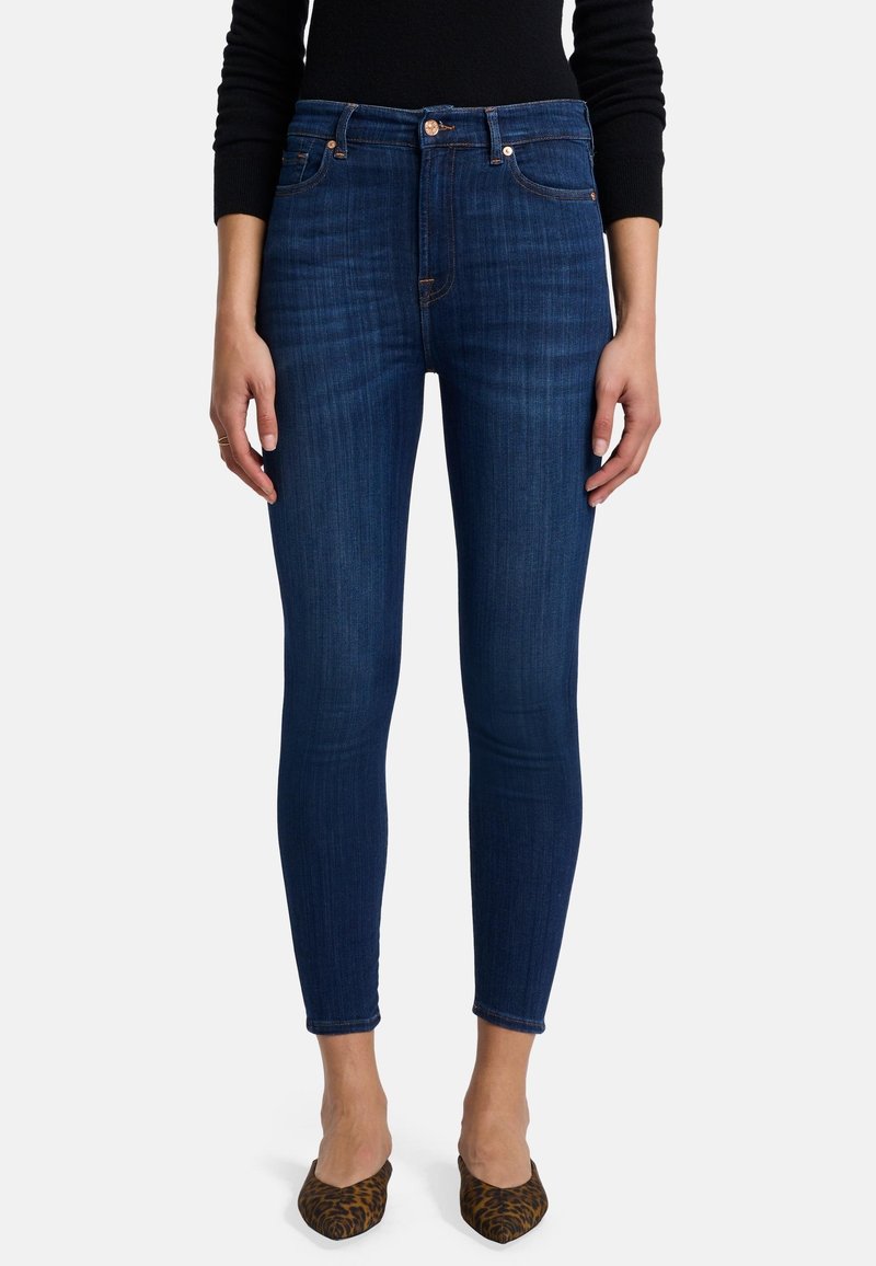 Jean skinny bleu foncé en denim avec une texture lisse. Doté d'une taille haute et d'un design à cinq poches. Associé à des chaussures à semelles pointues en imprimé léopard.