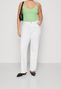 Top sin mangas verde ajustado con fruncidos en la parte delantera, combinado con pantalones anchos de talle alto blancos. Los accesorios incluyen un bolso negro pequeño y unos zapatos planos negros.