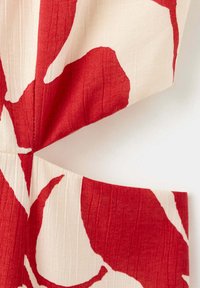 Gros plan sur un tissu rouge et blanc avec un grand motif floral abstrait et des coutures visibles sur un matériau texturé.