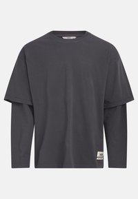 Tricou gri, cu mânecă scurtă, cu un design cu mânecă lungă suprapusă. Fabricat din bumbac, prezintă o etichetă a mărcii pe partea din față, în partea de jos.