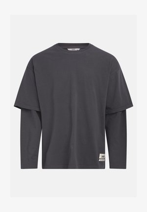 Hallikas lühikeste varrukatega t-särk, millel on kihiline pikkade varrukate disain. Valmistatud puuvillast, esiküljel on brändi silt.