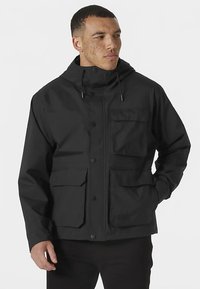 Jachetă neagră impermeabilă cu glugă, prevăzută cu mai multe buzunare frontale, capse și șnururi elastice pentru ajustarea potrivirii.