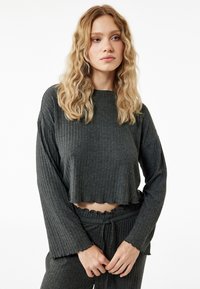 Donkergrijze, cropped top met lange mouwen in ribbeltextuur, met een gegolfde onderrand en een ontspannen pasvorm. Gecombineerd met bijpassende ribbelbroek.