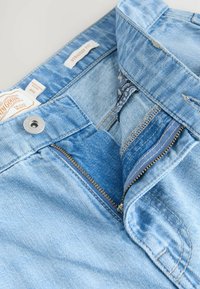 Jeans de mezclilla azul claro con un diseño de corte recto, que cuentan con un cierre de botón metálico, cremallera y detalles de tela interna en un azul más oscuro.