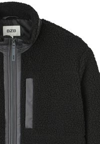Veste en polaire noire avec col montant, fermeture éclair à l'avant et poche poitrine avec bordure en tissu lisse.