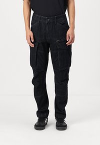 Black cargo pants with a textured fabric, featuring multiple pockets, a zippered pocket, and a straight-leg design.