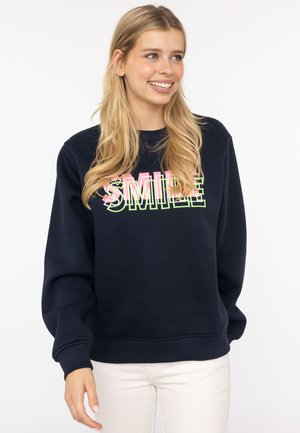 Navy Sweatshirt mit dem Aufdruck "SMILE" in pinken und grünen Buchstaben. Mit Rundhalsausschnitt und gerippten Bündchen. Der Hintergrund ist einfarbig weiß.