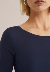 Temno modra rebrasta dolga majica z širokim izrezom, ki ima gladko teksturo in prilega silhueto.