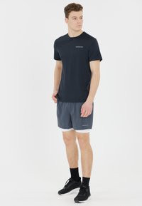 Granatowa koszulka z delikatnym logo, w połączeniu z szarymi spodniami sportowymi. Spodnie mają białą podszewkę i czarne buty sportowe.