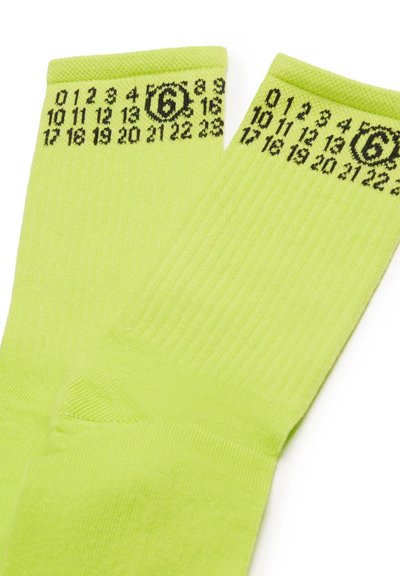 Calzini verde lime con texture a costine, caratterizzati da motivi numerici neri e un dettaglio grafico vicino alla parte superiore. Tessuto morbido.