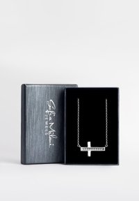 Collana a croce argentata con dettagli in zirconia cubica, esposta in una scatola di gioielli nera con un esterno grigio testurizzato.