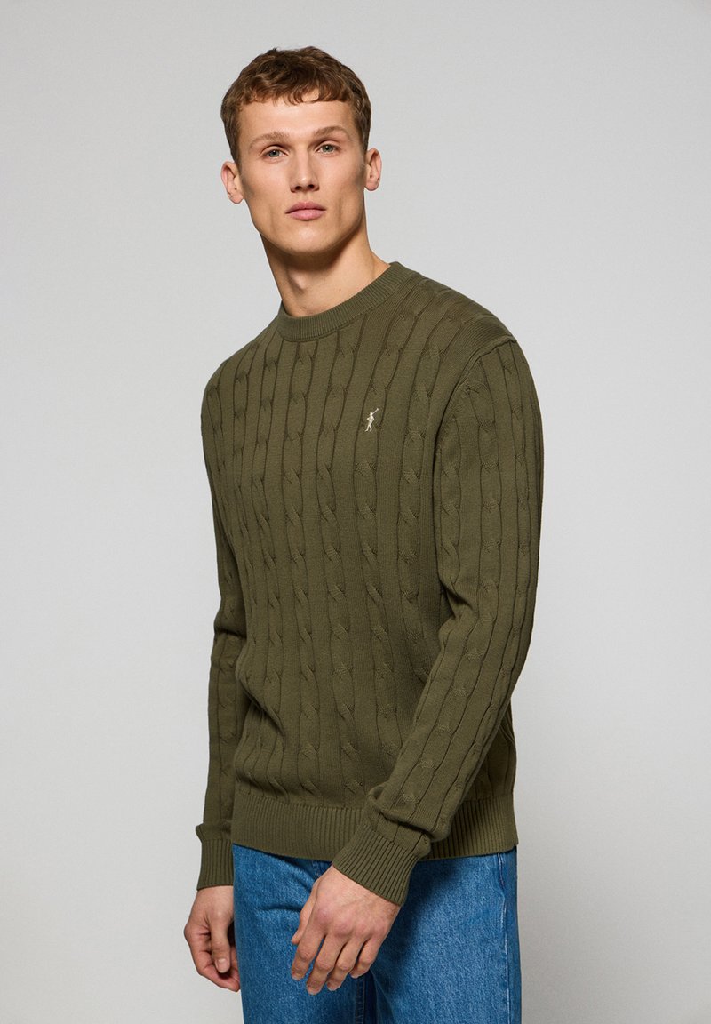 Olive green cable-knit sweater in textured fabric with ribbed cuffs and hem, featuring a small embroidered logo on the front.