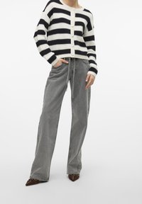 Randig stickad cardigan i svart och vitt med knappar, tillsammans med ljusgrå vida byxor och spetsiga bruna skor med nitar.