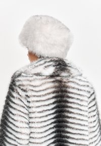 Cappotto in pelliccia sintetica con strisce bianche e nere, dotato di un morbido e soffice cappello bianco. Il tessuto texture crea un effetto stratificato.