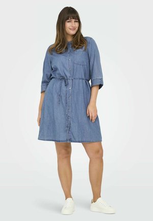Light blue, denim shirt dress with button-down front, belted waist, short rolled sleeves, and a single chest pocket. Paired with white sneakers.