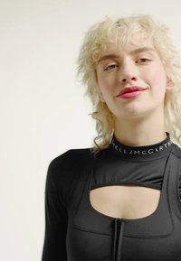 Black athletic bodysuit with a high collar, front zip, and cut-out detailing. Features stitching and a logo band at the neck.