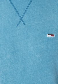 Polo shirt in cotone blu con una finitura testurizzata, caratterizzato da un design a punto X sul colletto e un piccolo logo in basso a sinistra.