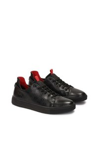 Zapatillas de cuero negro con un patrón texturizado, forro interior rojo y suela de goma negra. Incluye cordones negros y detalles decorativos.