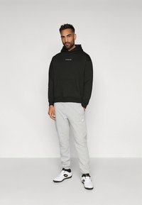 Sweat à capuche en coton noir avec poche kangourou, pantalon de survêtement gris et chaussures de sport blanches. Le sweat à capuche présente un petit logo sur la poitrine.