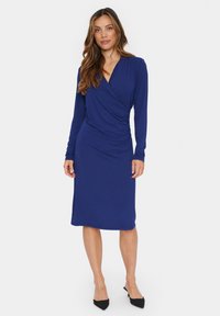 Sininen pitkähihainen kietaisumekko, jossa on slim fit -silhuetti, valmistettu pehmeästä kankaasta. Mekossa on rypytetty yksityiskohta vyötäröllä ja polveen ulottuva helma.