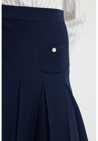 Falda plisada azul marino con cintura elástica, que cuenta con dos bolsillos. Cada bolsillo tiene un detalle de botón dorado circular. Tejido suave y texturizado.